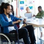 Man in wheelchair using tablet in meeting.