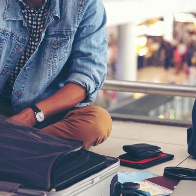 A male traveler is sitting on the ground of an airport while fixing items from his travel bags.