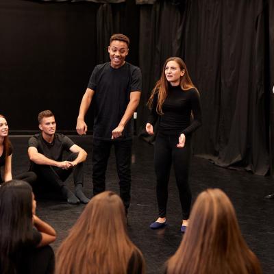 A teacher and a group of drama students rehearsing during a performing arts class.