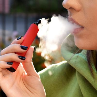 close up of someone exhaling smoke from vaping, holding vape with black nail polish on fingernails.