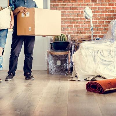 Torso view of two people standing by door moving in items to new home with a brick interior wall on the right.