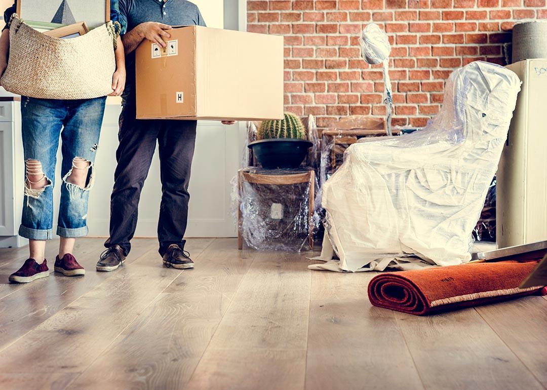 Torso view of two people standing by door moving in items to new home with a brick interior wall on the right.