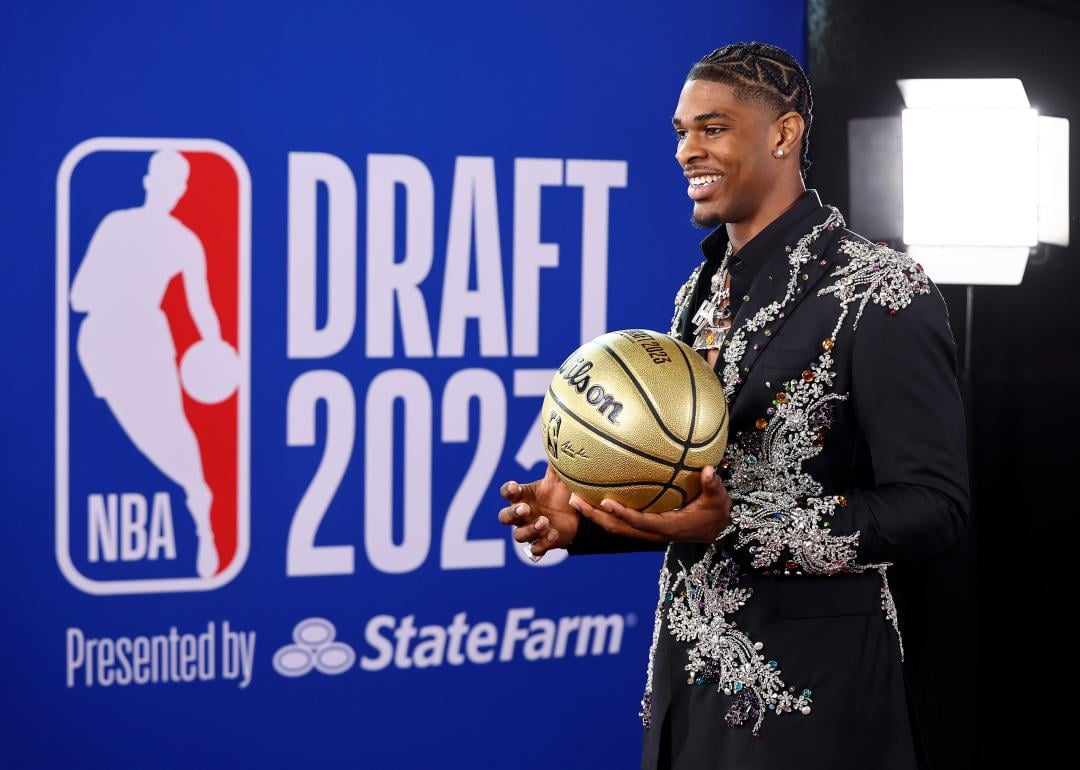 Scoot Henderson holding a golden basketball standing in front of a backdrop for the 2023 NBA Draft.