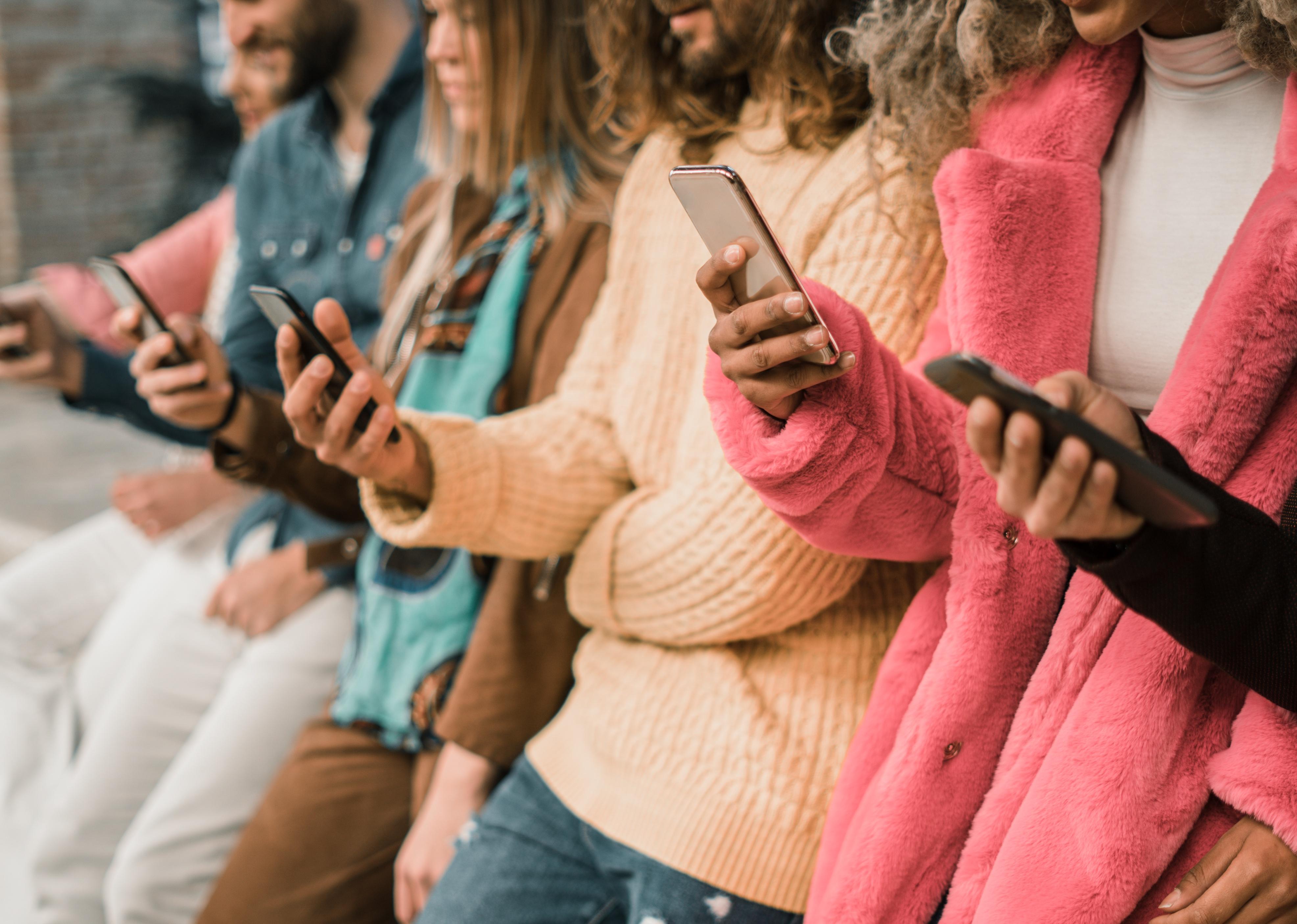 Group of young people using smartphone sitting in a bench.