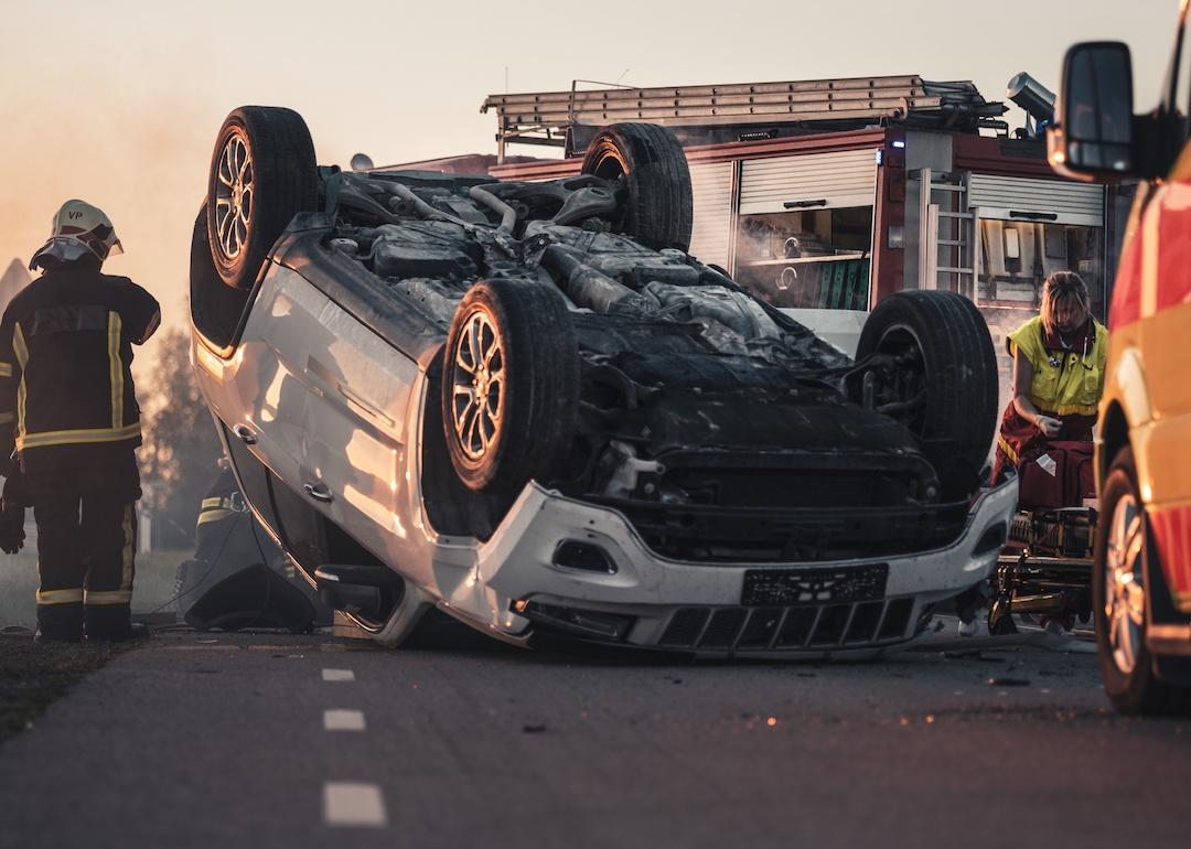 Burning vehicle upside down in the middle of the road after collision.