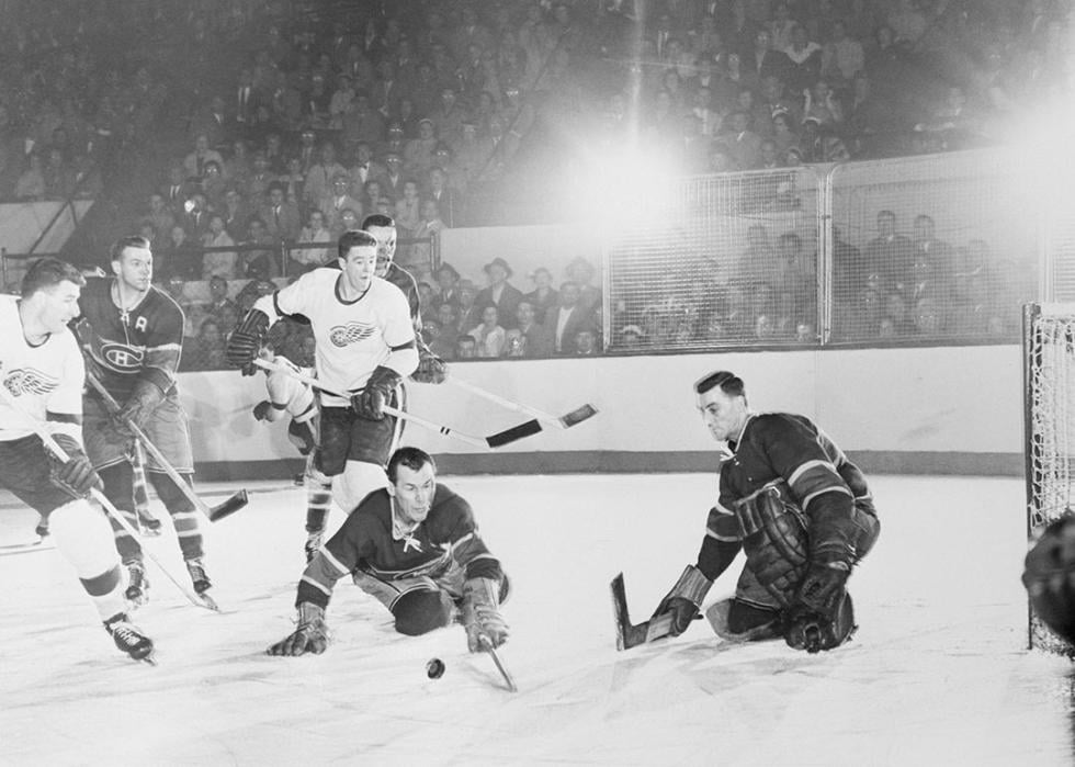 Canadiens' Butch Bouchard and goalie Jacques Plante (right) in the first game of the Stanley Cup series at Detroit. Other players are (from left): Vic Stasium, Detroit Red Wings; Ken Mosdell, Canadiens; Marcel Pronovost, Red Wings; and Tom Johnson, Canadiens (rear). The Wings won, 4-2.