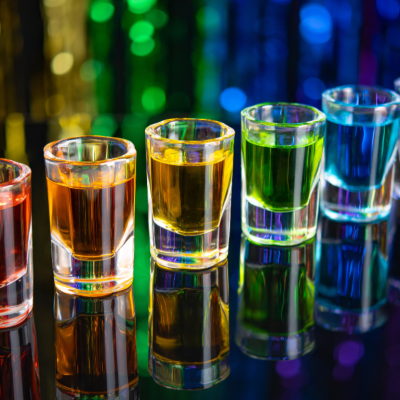 A rainbow of shot glasses on a bar.