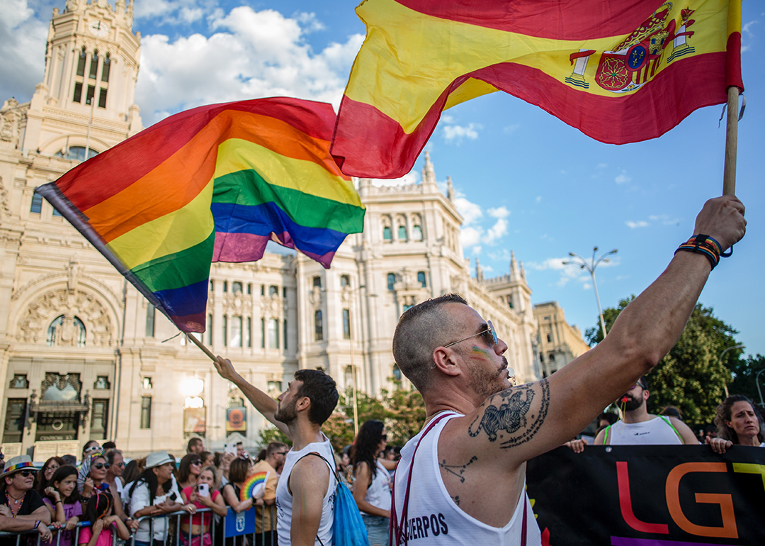 A man waves the Spanish flag and another the LGTBI+ flag in front of the Palacio de Cibeles, during the Pride March in Madrid.