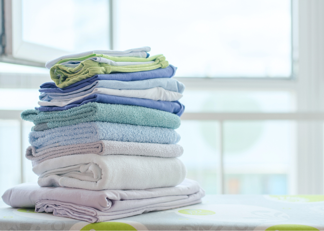 A stack of folded clean laundry sites on an ironing board.