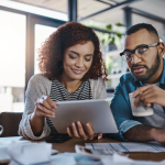 a man and woman at a table look over documents and tablet 