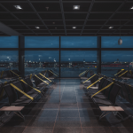 A wide-angle view of a dark empty abandoned quarantined waiting hall of a modern airport terminal at night, on a lockdown with regular greenish tapes over the seats to maintain social distancing