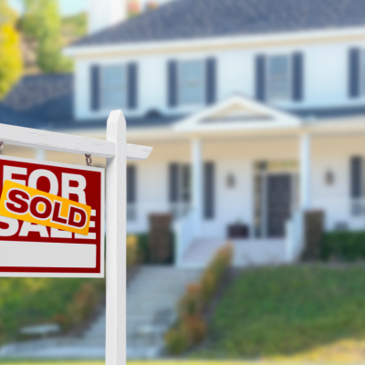 A for sale sign with a sold sticker in front of a suburban home.