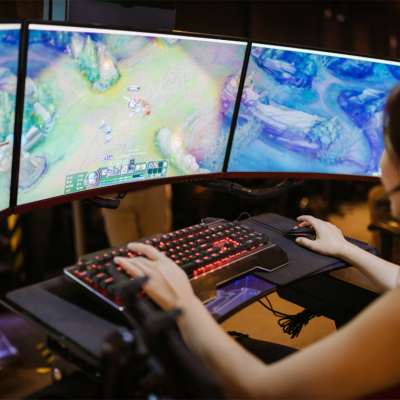 A female gamer is focused playing a PC game displayed on three monitors.