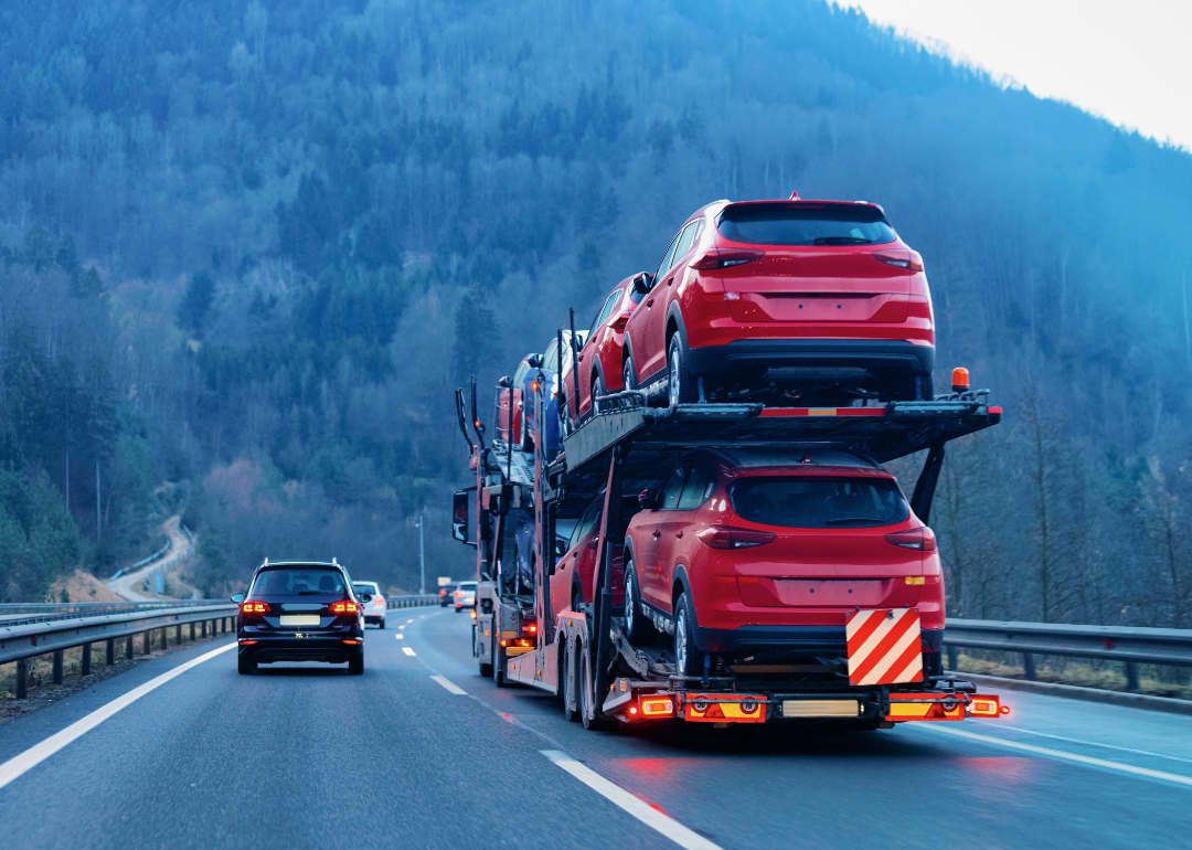 Cars carrier transporter truck drives on road with tree-covered mountains in the distance.