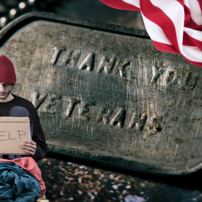 A man is seated against a backdrop of a military dog tag and an American flag.