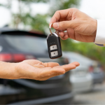 one person handing over car keys to another with cars in background